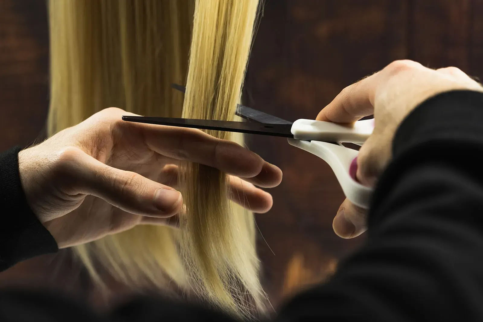Mani che tagliano a forbice una ciocca di capelli biondi